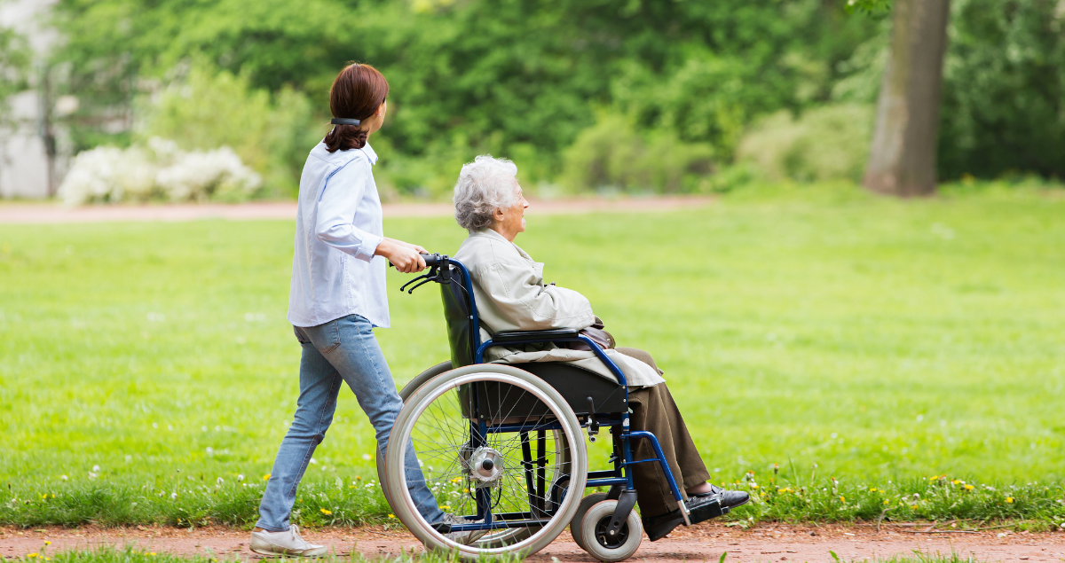 A woman pushing an older woman in a wheelchair at a long term care facility