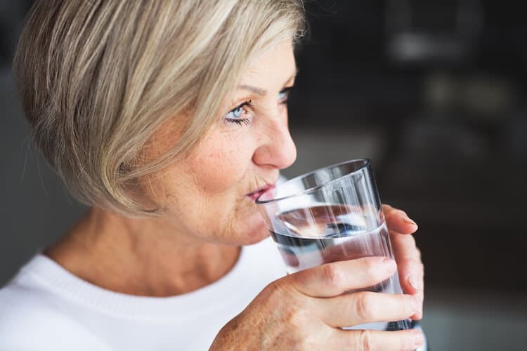A senior woman enjoys a glass of refreshing water to stay hydrated.