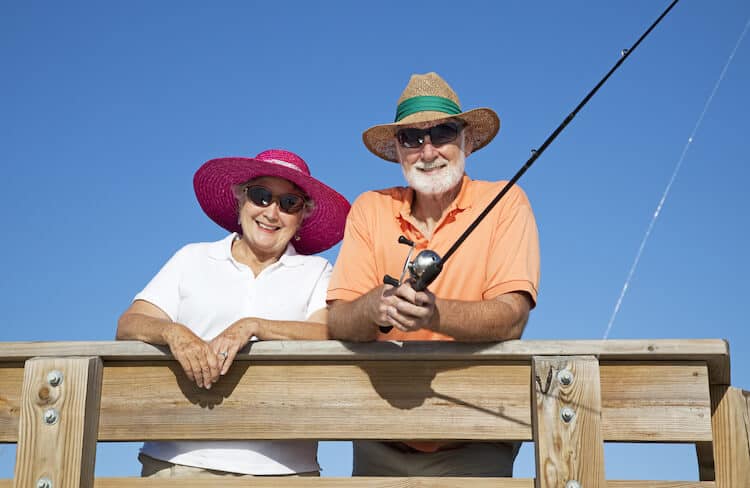 Senior couple protects themselves from the sun while fishing, using hats and sunglasses.