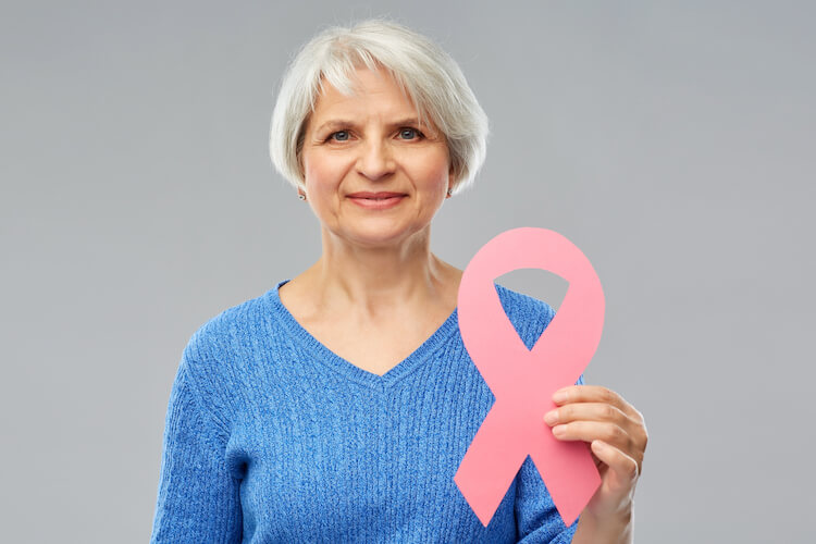 A smiling senior woman holds a pink ribbon for breast cancer awareness month.