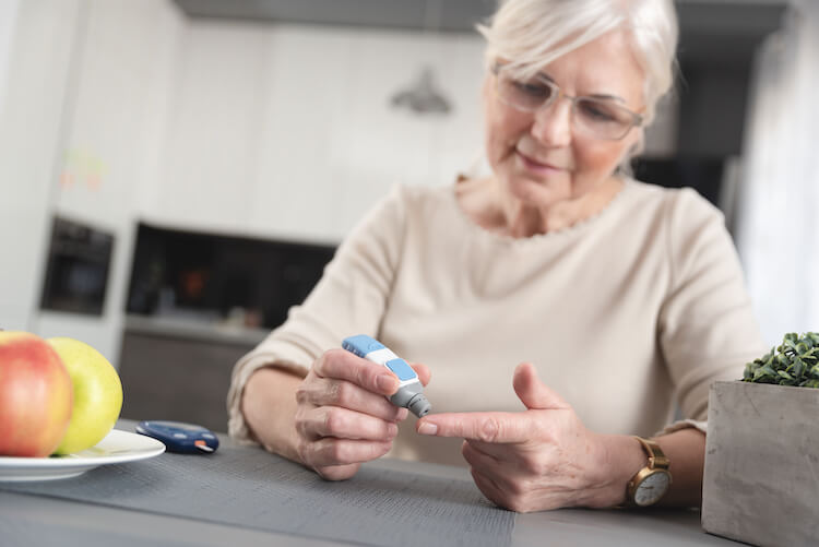 A smiling senior woman checks her blood glucose level for Diabetes Awareness Month.