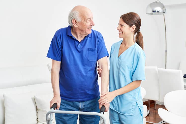 A occupational therapist helping a senior man walk.