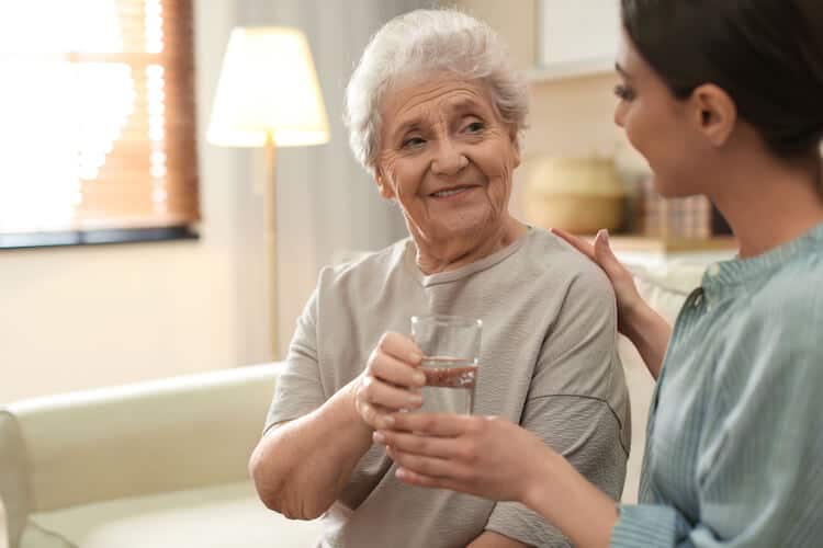 A family caregiver offers water to her senior loved one.