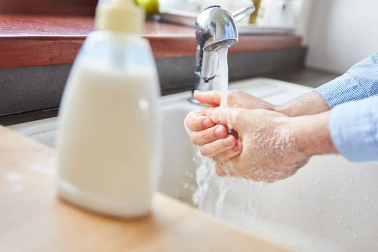 Elderly woman washing hands with liquid soap at home at the sink.