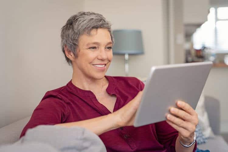 Smiling senior woman looking at her digital tablet while sitting on sofa.