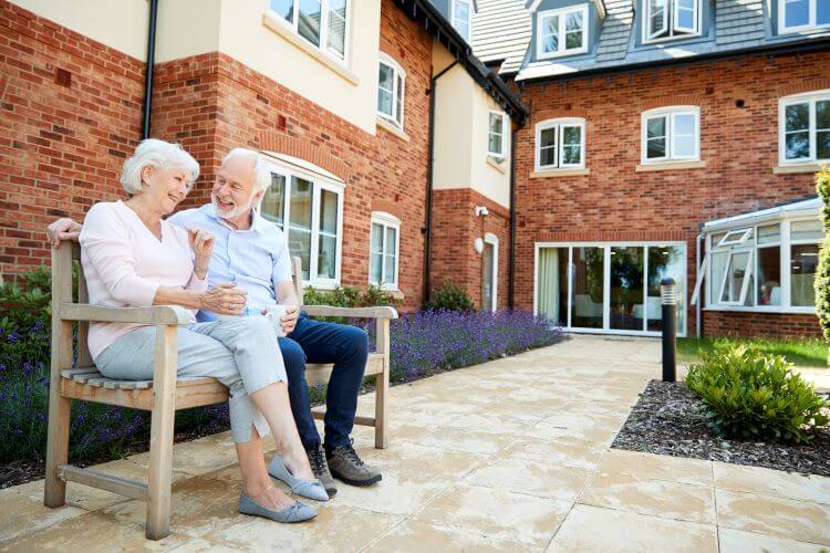 Retired couple sitting on bench with hot drinks in their hands in assisted living facility.