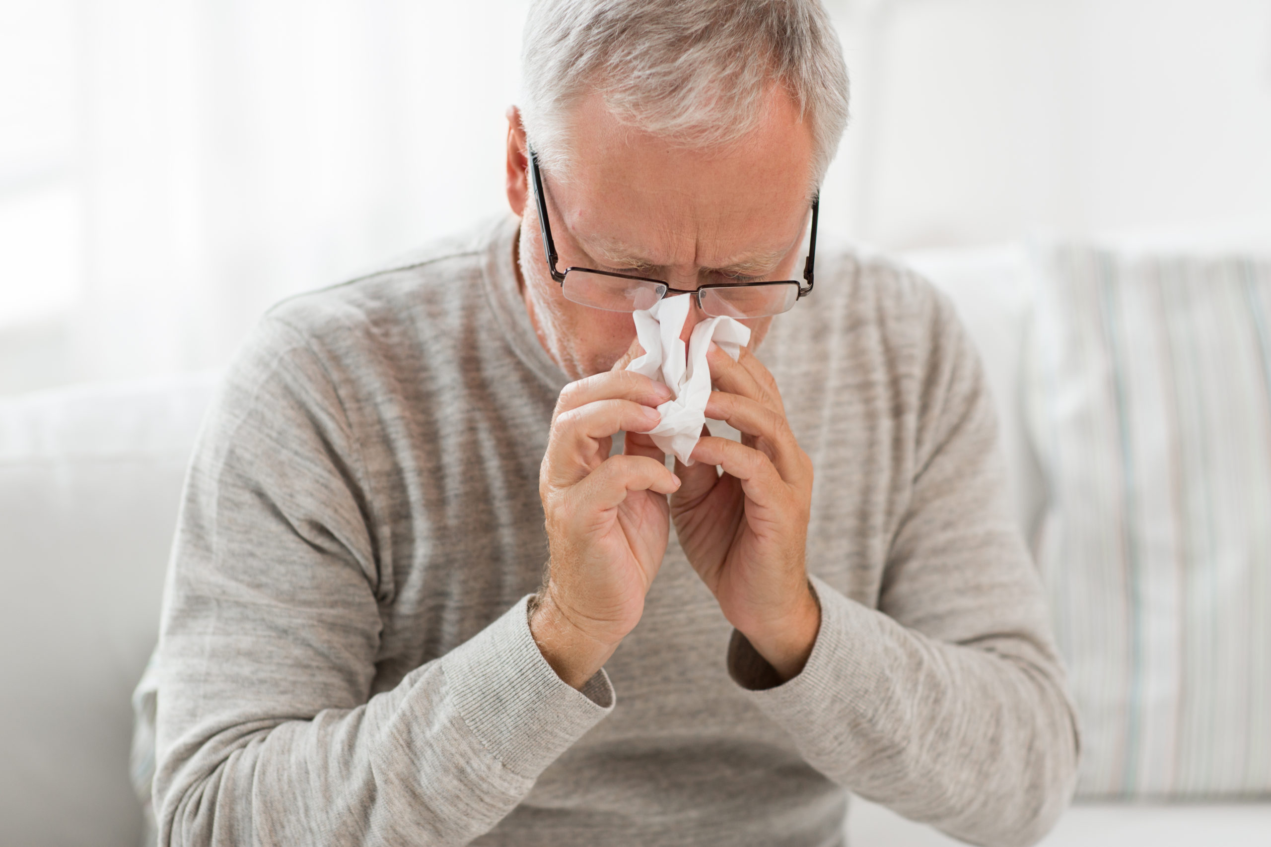 Senior man blows his nose due to allergy symptoms.