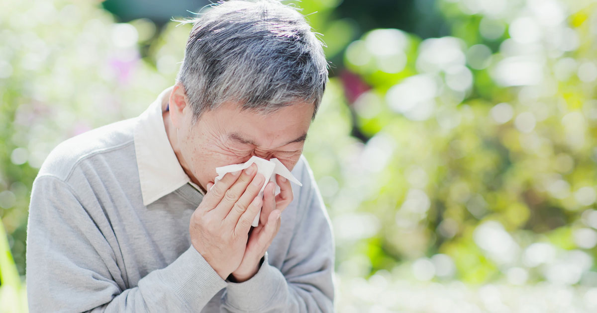 A senior man sneezing into a tissue