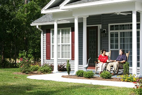 Advent Christian Village members sitting on the porch of their Tudor-style house.