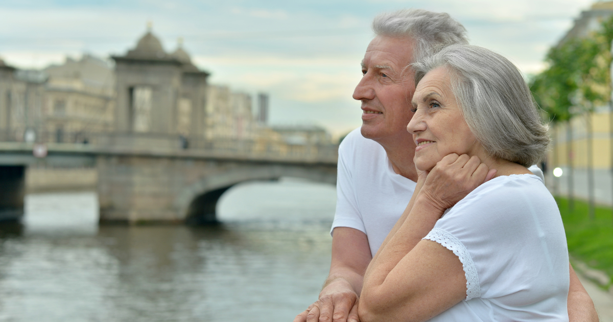 A picture of two older adults, a man and a woman, enjoying a view by the water on vacation.